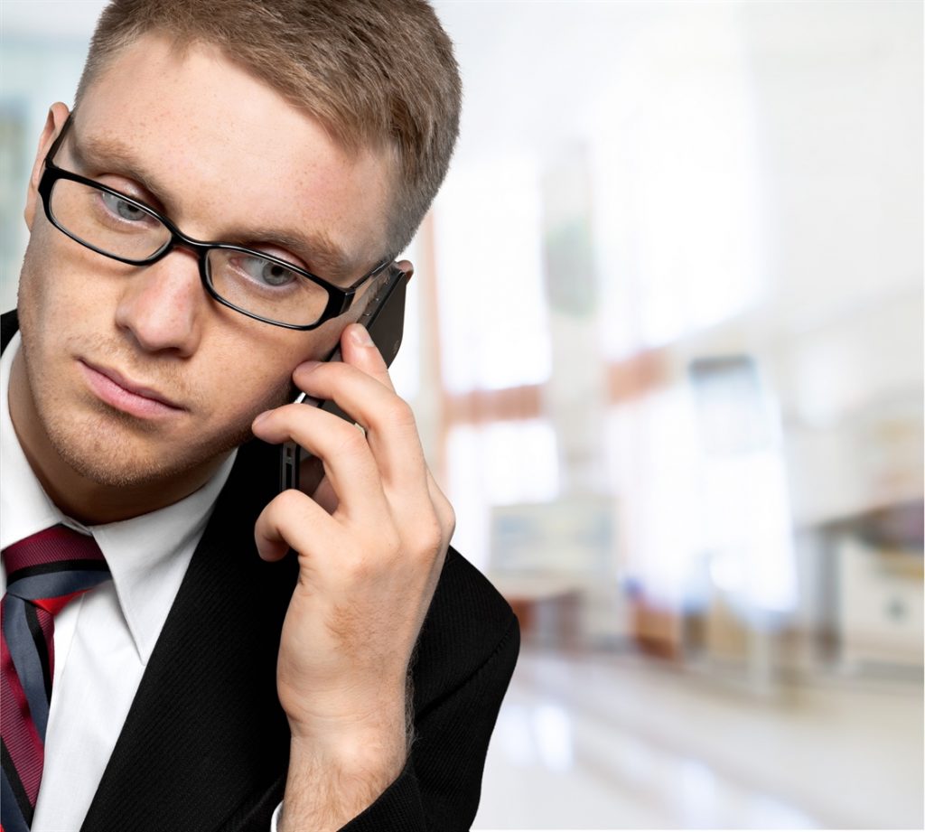 Hombre con traje y lentes contestando una llamada con su móvil en el oído